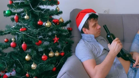 Portrait man drinking wine from bottle on couch near Christmas tree, side view. Stock Footage 137524791