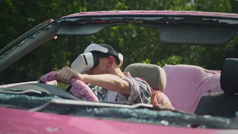 Portrait of man driving a broken pink convertible with a virtual reality headset Stock Footage 236848061