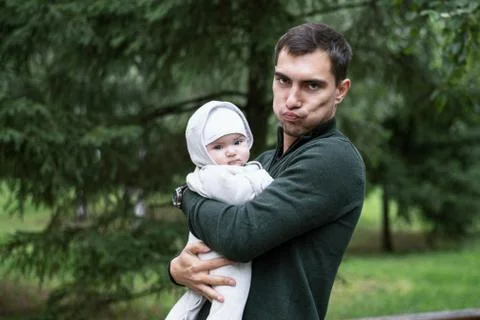 Portrait of man in green jacket making faces with child in his arms in Park i Stock Photos