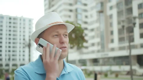 Portrait of a man in a hat talking on a mobile phone, urban background 스톡 동영상 151215988