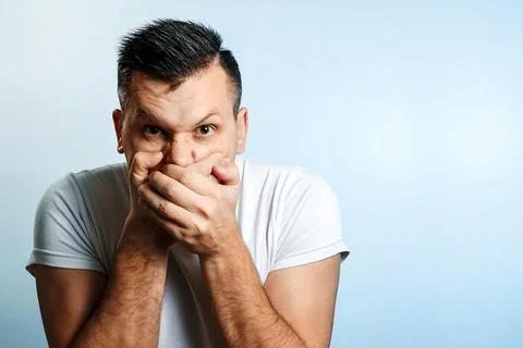 Portrait of a man on a light background, covers his mouth with his hands, cen Stock Photos