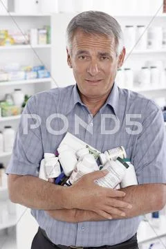 Portrait Of Man In Pharmacy Carrying A Pile Of Pill Bottles