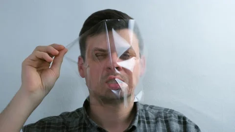 Portrait of man is puttion on plastic transparent film on his face. Video stock 152712848
