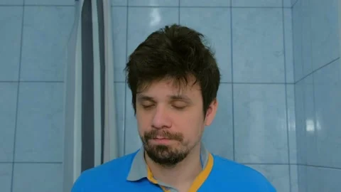 Portrait of man shaves beard using electric razor in bathroom looking at camera. Video stock 136033901
