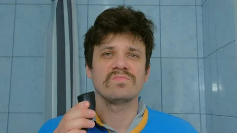 Portrait of man shaves beard using electric razor in bathroom looking at camera. Stock Footage 136425129