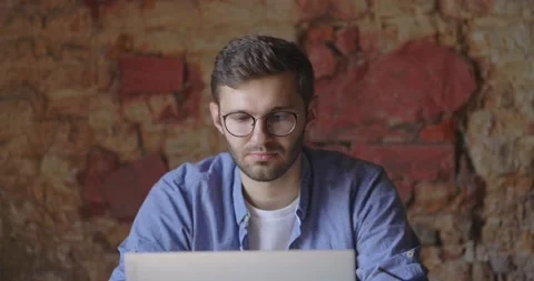 Portrait of man sits and using the laptop for the remote work at concrete wall Stock Footage 166302317