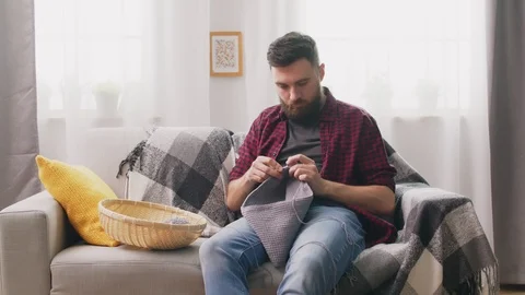 Portrait of man sitting on couch and knitting at home Video stock 107348986