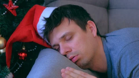 Portrait of man sleeping lying on couch near Christmas tree at eve in red cap. Stock Footage 136051632