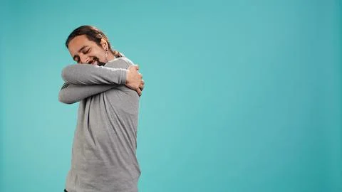 Portrait of man standing in studio, hugging himself, doing self love Stock Photos