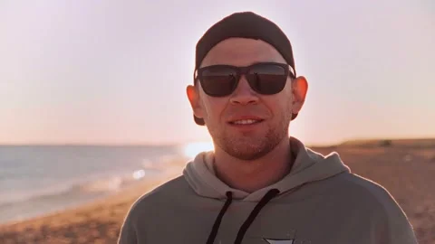 Portrait of man in sunglasses smiling at camera standing on sandy beach Stock Footage 185774174