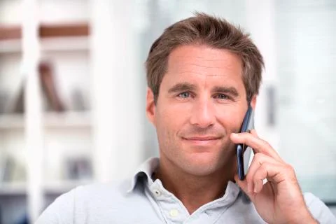 Portrait of a man using a cell phone while sitting on a sofa at home, smiling Stock Photos