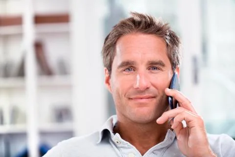 Portrait of a man using a cell phone while sitting on a sofa at home, smiling Stock Photos