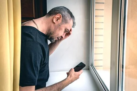 Portrait of a man using a smartphone in front of a window. Upset man reading  Stock Photos