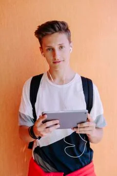 Portrait of man using tablet computer while standing against orange wall at 스톡 사진
