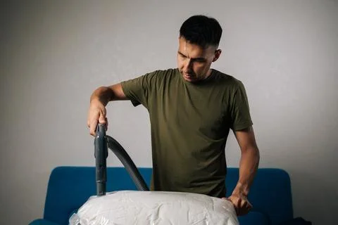 Portrait of man using vacuum cleaner to extract air from storage bag filled with Stock Photos