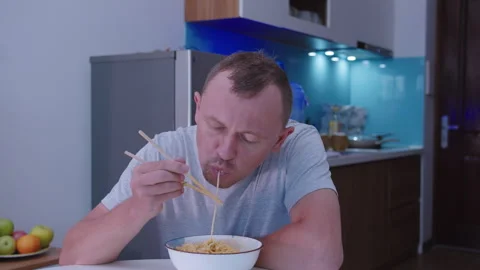 Portrait of a man who eats simple ramen noodles with chopsticks from a cup Vídeos de archivo 331140228