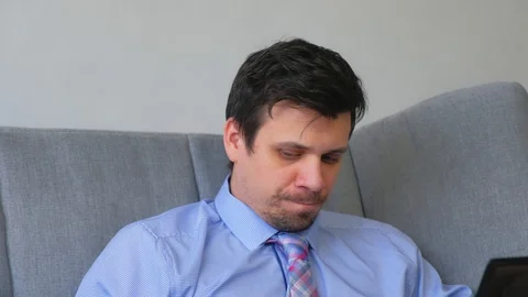 Portrait of man working on laptop talking smartphone sitting on couch at home. Stock Footage 128966137