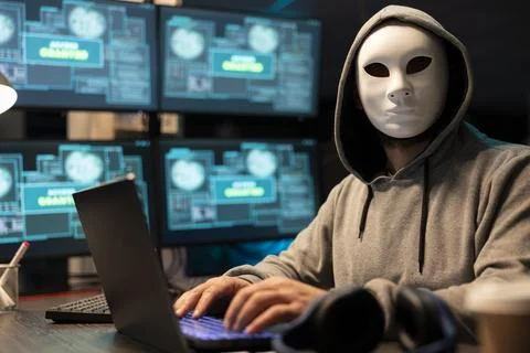Portrait of Masked Hacker Operating Laptop in Dark Tech Room Stock Photos