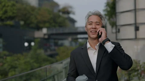 Portrait of mature Asian man talks on smartphone and holds coffee in downtown Stock Footage 319892453