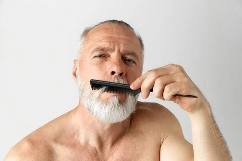 Portrait of mature handsome man with gray hair taking care after beard, brushing Stock Photos