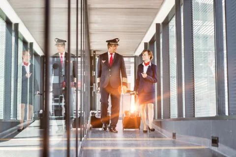Portrait of mature pilot walking with young attractive stewardess in airport Stock Photos