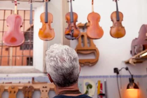Portrait of mature violin maker while looking the violins in his laboratory Stock Photos