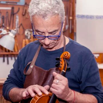 Portrait of mature violin maker while testing the violins in his laboratory Stock Photos