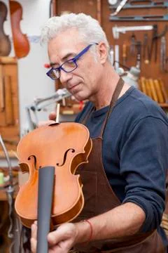 Portrait of mature violin maker while testing the violins in his laboratory Stock Photos