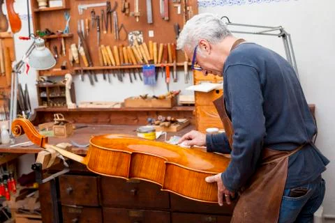 Portrait of mature violin maker while testing the violins in his laboratory Stock Photos