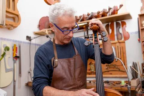 Portrait of mature violin maker while testing the violins in his laboratory Stock Photos