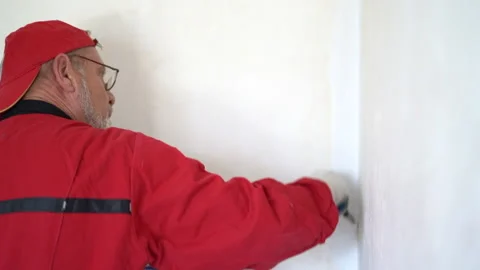 Portrait of a mature worker in a red cap and overalls painting the wall Stock Footage 167264305