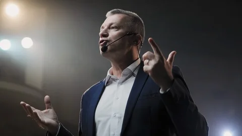 Portrait of men speaking through a microphone in dark conference hall. Person Видео 121587210