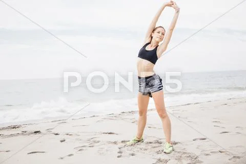 Portrait Of Mid Adult Woman Standing On Beach, Hands Over Head, Stretching