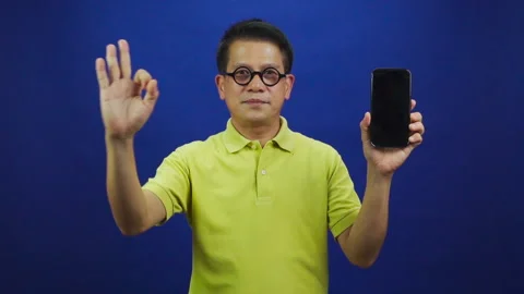 Portrait of middle-aged asian man showing smartphone and giving ok sign Stock-Footage 219469261