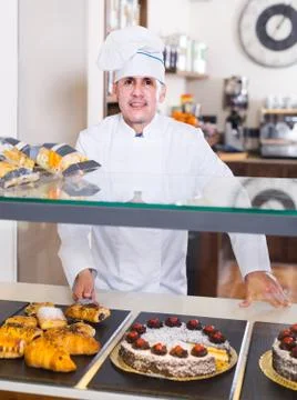 Portrait of middle aged man baker with tasty cakes smiling in bakery Stock Photos