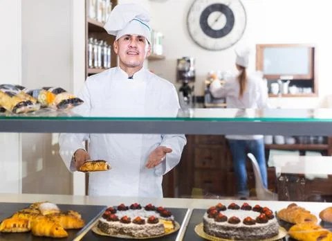 Portrait of middle aged man baker with tasty cakes smiling in bakery Stock Photos