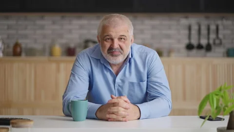 Portrait of middle-aged man sitting at kitchen and looking at camera, video chat Stock Footage 153515427