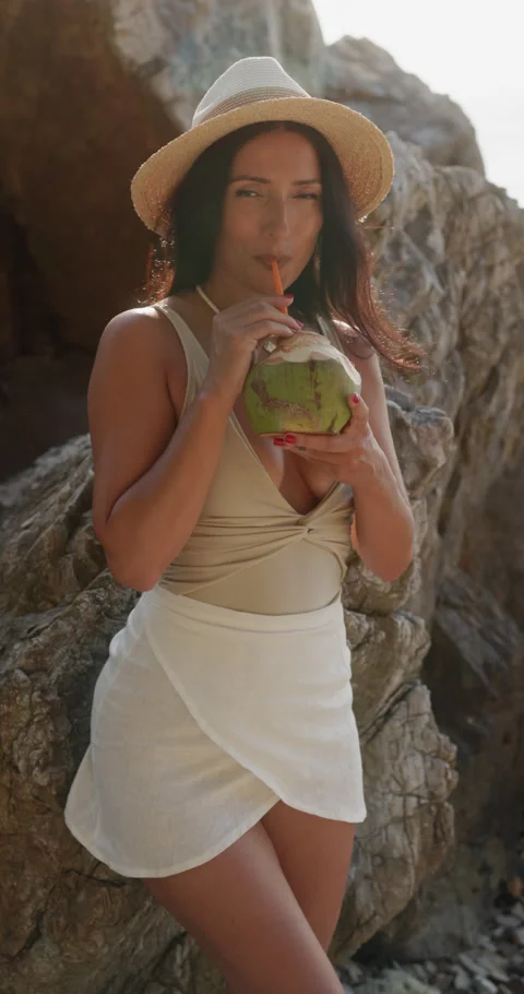 Portrait of Middle Eastern woman drinks fresh coconut near rugged coastal rocks Stock Footage 346650375