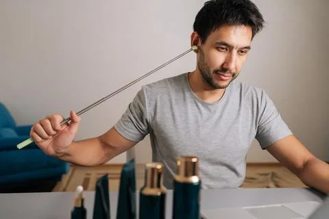 Portrait of millennial man scratching ear with back scratcher working from home Stock Photos