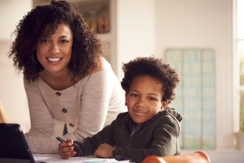 Portrait Of Mother Helping Son With Homework Sitting At Kitchen Counter Using Stock Photos