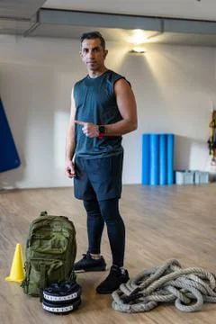 Portrait of motivated boot camp instructor in gym hall. Rope, dumbbells and s Stock Photos