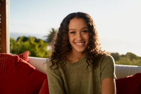 Portrait of Multicultural female smiling while sitting on sofa in living room of Stock Photos