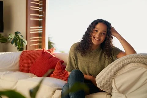 Portrait of Multicultural female smiling while sitting on sofa in living room of Stock Photos