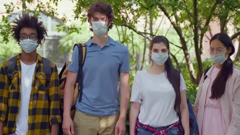 Portrait of multiethnic students put on safety mask looking at camera outdoors Stock Footage 244511124