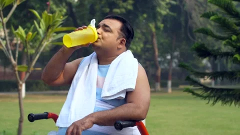 Portrait of an obese indian man sitting in a park and drinking water - hydrat... Video stock 264015953