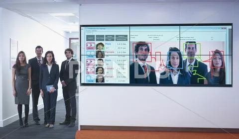 Portrait Of Office Workers Standing Next To Face Recognition Software System