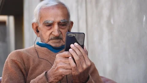 Portrait of old Indian businessman using mobile phone with ear phones. Watching  Stock Footage 146375596