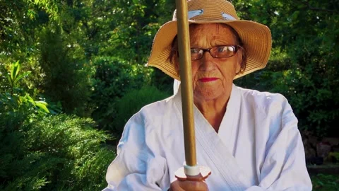 Portrait of an old lady training with a katana in the garden. Camera movement. Stock Footage 310332849