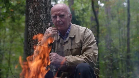 Portrait of an old man in the forest warming himself by the fire looking and Stock Footage 159852510
