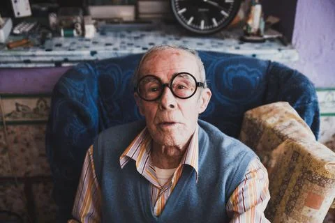Portrait of an old man with glasses sitting on the sofa at home. Stock Photos